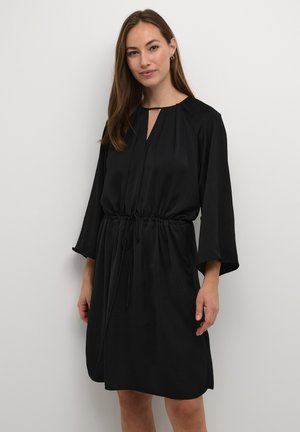 Zwarte jurk van soepel stof, met een trekkoord in de taille, brede mouwen en een sleutelgatopening bij de hals.