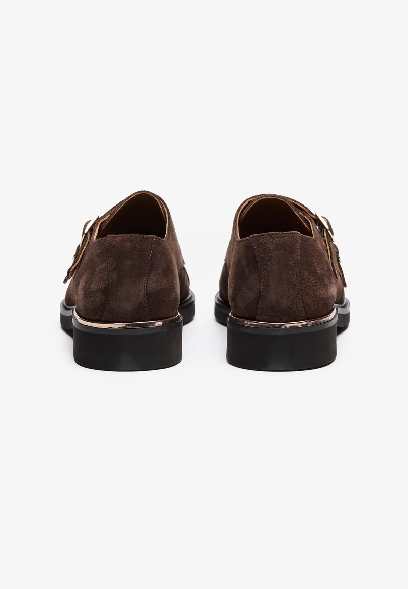 Chaussures en daim marron avec des talons ronds, présentant un accent brillant autour de la semelle et un détail à double boucle sur chaque chaussure.