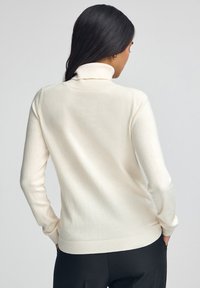 Maglione a collo alto color crema chiaro, realizzato in tessuto morbido, con maniche lunghe, polsini e orlo a coste, con una silhouette aderente.