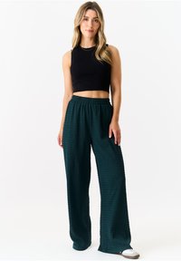 Black cropped tank top paired with green textured wide-leg pants. The pants have an elastic waistband and a loose fit.