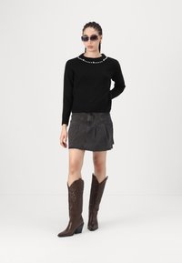 Črn pulover z bisernim obrobnim pri ovratniku, siva jeans krilo in rjavi usnjeni škornji do kolen s koničastimi prsti in teksturiranim dizajnom.