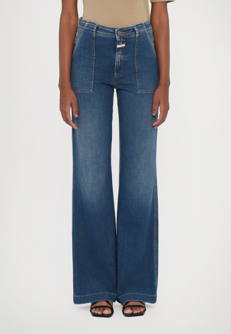 Høyt liv, vide jeans i medium blå denim. Har frontlommer, knappest closure, og subtil fading langs bena.