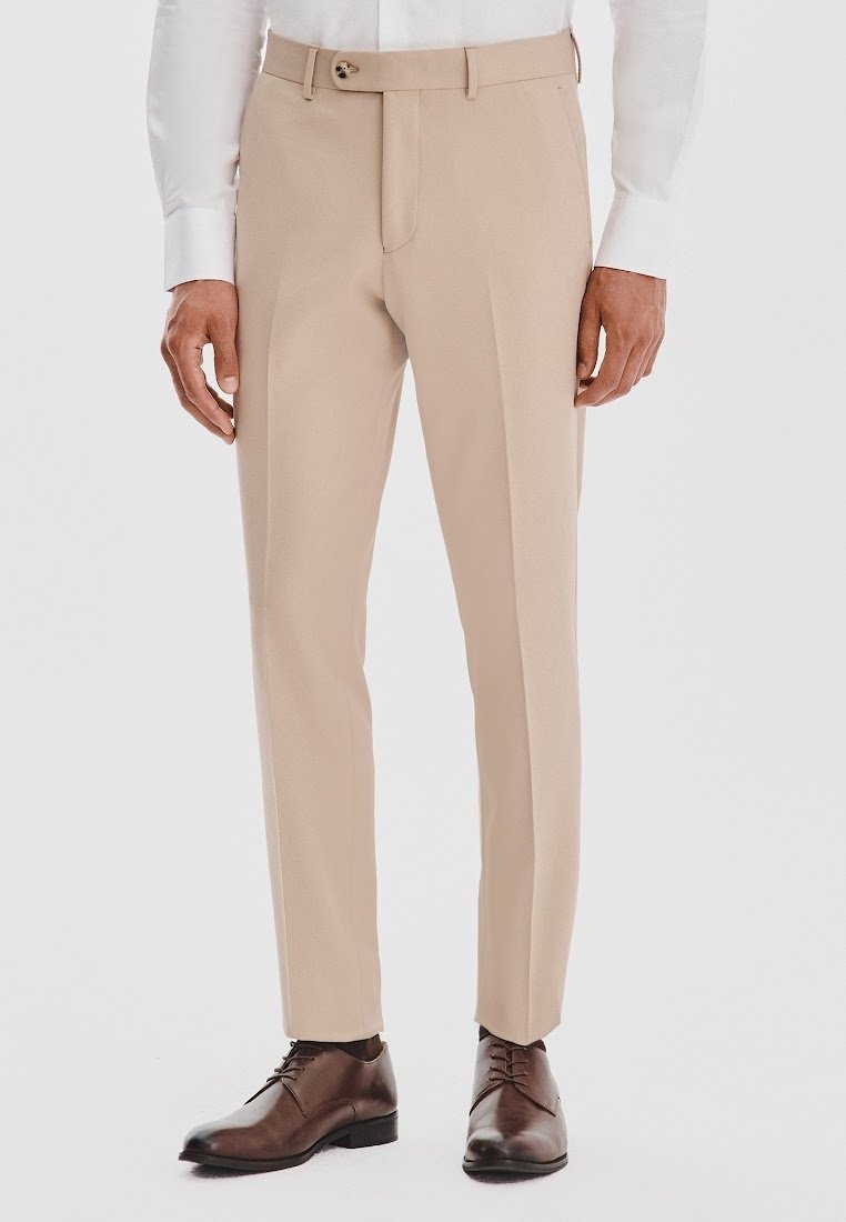 Beżowe spodnie dopasowane z płaskim przodem, z szlufkami na pasek i pojedynczym zapięciem na guzik; w połączeniu z brązowymi skórzanymi butami i białą koszulą.