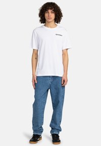 Hvid bomulds T-shirt med korte ærmer og trykt "ELEMENT" logo. Kombineret med løstsiddende lyseblå denim jeans og sorte sneakers.