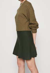 Suéter de punto verde oliva con un diseño texturizado, combinado con una falda acampanada verde oscuro. Ambas prendas presentan dobladillos acanalados.