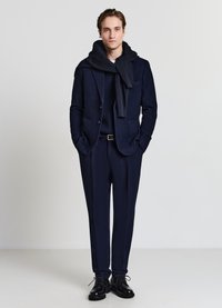 Marineblauer Anzug mit einem darunter getragenen, gerippten Pullover, kombiniert mit einem passenden Schal. Schwarze Schnürschuhe vollenden den formellen Look des Outfits.