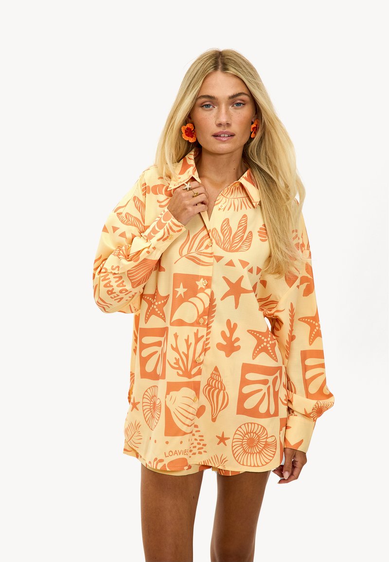 Chemise boutonnée en jaune clair avec des motifs marins corail. Comprend un col, des manches longues et une coupe décontractée. Tissu texturé.