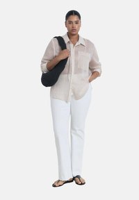 Camicia a righe nelle tonalità beige chiaro e bianco, abbinata a pantaloni bianchi a gamba dritta e borsa a tracolla nera intrecciata. Sandali bassi completano il look.