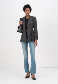 Siv pinstripe blazer čez črn top, v kombinaciji z svetloblujimi flare jeans in črnimi petami. Vključuje majhen črn ročni torbico.