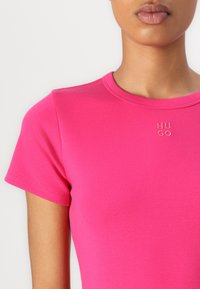 T-shirt en coton rose ajusté à manches courtes et décolleté rond, avec un logo "HUGO" embossé discrètement sur le devant.