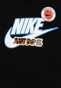 Felpa nera con un grande logo blu Nike e "JUST DO IT" in rosso. Include una toppa rotonda con una faccia sorridente e del testo.