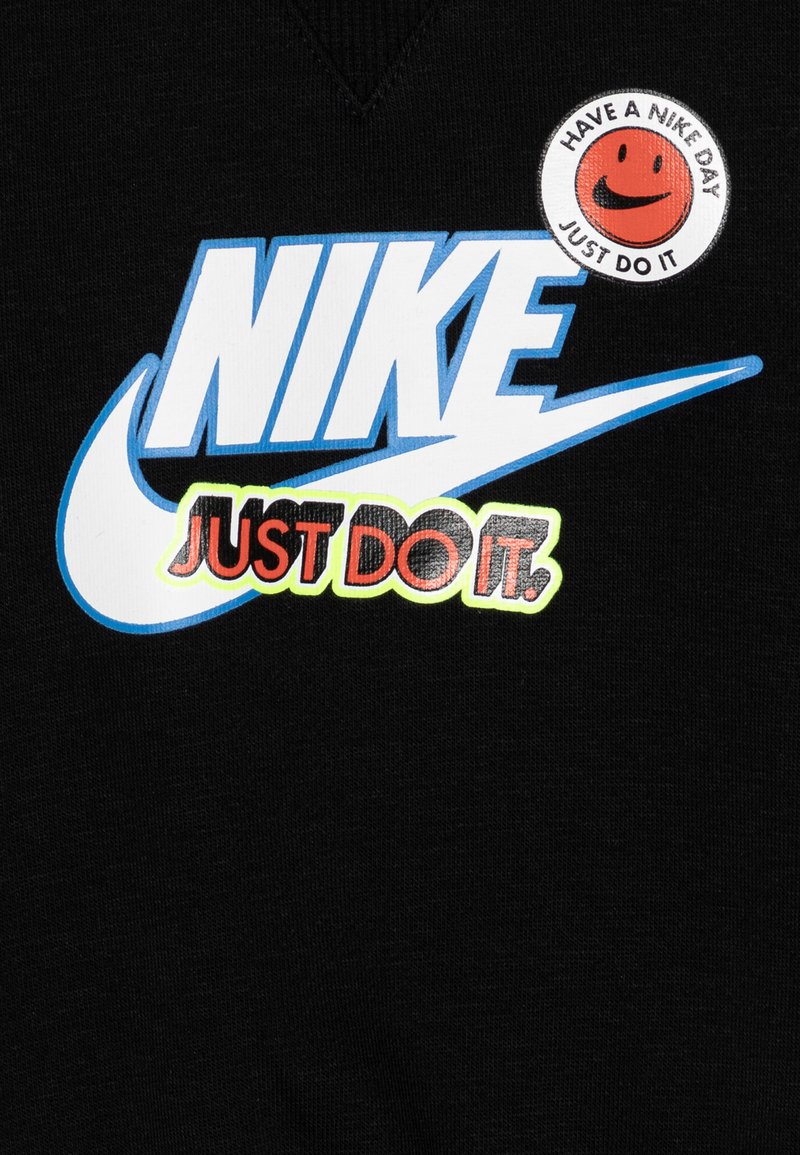 Schwarzer Sweatshirt mit einem großen blauen Nike-Logo und "JUST DO IT" in Rot. Enthält ein rundes Patch mit einem lächelnden Gesicht und Text.