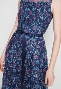 Robe marine avec broderies florales en rose et bleu, dotée d'un décolleté transparent, d'un corsage ajusté et d'une ceinture en satin à la taille.