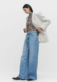 Beige blazer over een bruine slangenprint top, gecombineerd met oversized blauwe spijkerbroeken en zwarte schoenen. Zachte texturen met een losse pasvorm.