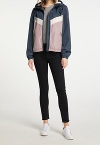 Giacca leggera a blocchi di colore in navy, rosa e crema, con cappuccio, polsini elasticizzati e zip frontale. Abbinata a pantaloni neri e sneakers bianche.