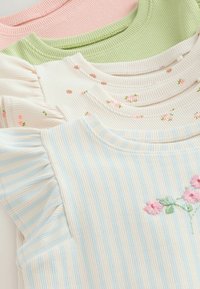 Cuatro tops de punto acanalado en rosa pastel, verde, crema con estampados florales y rayas azul-blancas con bordado floral, ordenadamente apilados.