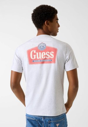 Grijs T-shirt met korte mouwen met een groot rood-wit "Guess Jeans Company" logo op de achterkant, gemaakt van een zachte, gestructureerde stof.