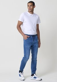 Pantalones jogger de denim azul con cintura elástica y puños, que presentan una textura suave y costuras en contraste. Combinados con una camiseta blanca lisa.