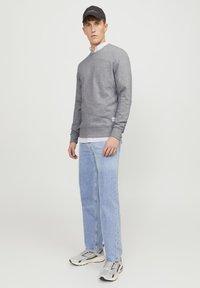 Gray sweatshirt with ribbed cuffs and a v-neck, layered over a striped shirt. Paired with light blue jeans and gray sneakers. Black cap.