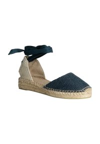 Espadrille azul tejido con parte trasera de lona beige, suela de yute y cintas de raso azul marino alrededor del tobillo. Presenta un diseño de cuña baja.