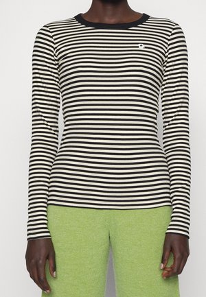 Personne portant un t-shirt à manches longues rayé horizontalement noir et blanc avec un petit détail de fleur et un pantalon vert clair.