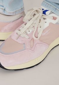 Pink sneakers with a mix of suede and mesh materials. Features cream laces, a white and blue logo, and a yellow sole with a textured black bottom.