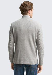 Pull en tricot gris avec un col haut et des accents en tricot torsadé sur les manches. Texture côtelée et design ajusté.