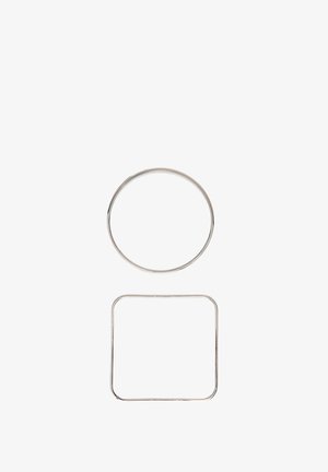 Jeden strieborný kruhový kovový prsteň nad jedným strieborným štvorcovým kovovým prsteňom s zaoblenými rohmi na bielom pozadí.