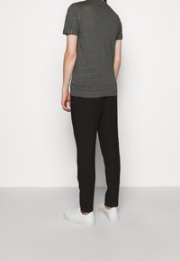 T-shirt grigio a maniche corte con una texture liscia, abbinato a pantaloni neri attillati e sneakers bianche, visto da dietro.