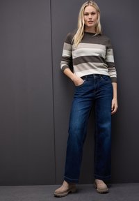 Sweter w paski w odcieniach brązu i beżu, zestawiony z ciemnoniebieskimi spodniami o szerokich nogawkach i beżowymi botkami za kostkę. Prosty wzór, miękka tekstura.