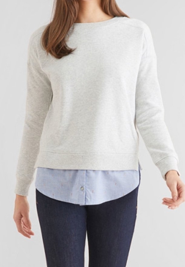 Sweatshirt gris clair à encolure ronde et manches longues, superposé sur une chemise boutonnée bleu clair, associé à un jean bleu foncé.