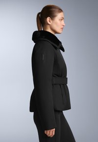 Crna podstavljena jakna s ovratnikom od umjetnog krzna, pojasom u struku i glatkim, teksturiranim materijalom. Ima logo na rukavu i strukturirani siluetu.
