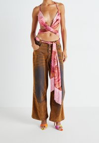 Hnědé kalhoty širokých nohavic se vzorovaným šátkem uvázaným v pase. Růžový zavinovací top s tenkými ramínky. Barevné sandály s otevřenou špičkou.