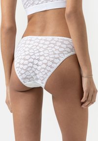 Culotte en dentelle blanche avec un motif floral, taille élastique et bordure festonnée, offrant un ajustement serré et une texture douce.