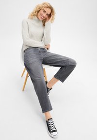 Pull à col roulé gris côtelé associé à un jean gris ample, avec un ourlet court et des poches latérales, complété par des baskets noires.