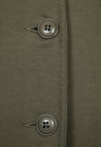 Olive green fabric with ribbed texture, featuring two large circular buttons and visible stitching along the edge.