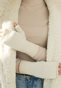 Jasnobeżowe rękawiczki bez palców o prążkowanej strukturze i miękkim wykończeniu, noszone na dopasowanym beżowym golfie i puszystej, kremowej kurtce.