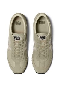 Beiga sportskor med ett texturerat läderöverdrag, vita detaljer och snörningsdesign. Gummisula med synligt mönster.