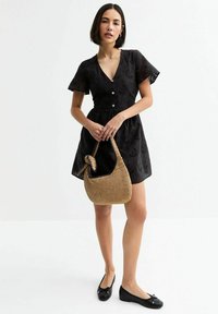Black short-sleeve dress with a v-neck, button front, and floral embroidery. Paired with a woven tan bag and black ballet flats.