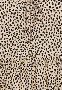 Beige klänning med ett mönster av svarta prickar, med en samlad knytkrage och en gathered nederkant, tillverkad av ett mjukt tyg.