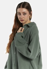 Langærmet, grøn struktureret skjorte med knap og krave samt oversized pasform. Stoffet ser blødt og let krøllet ud.