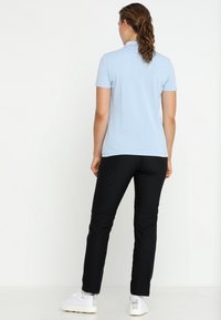 Ljusblå pikétröja med ett strukturerat mönster kombinerad med svarta, raka byxor; modellen bär vita sneakers.