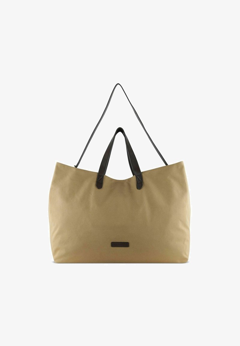 Sac fourre-tout en toile beige avec poignées en cuir noir ; forme spacieuse et rectangulaire ; design minimaliste avec un petit patch logo.