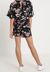 Mono corto negro con flores de manga corta, con una abertura en la parte posterior y un vibrante estampado floral en tonos rosa y verde.