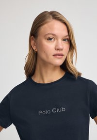 Camiseta de algodón navy con mangas cortas y cuello redondo, que presenta "Polo Club" en Strass en el pecho. Textura suave.