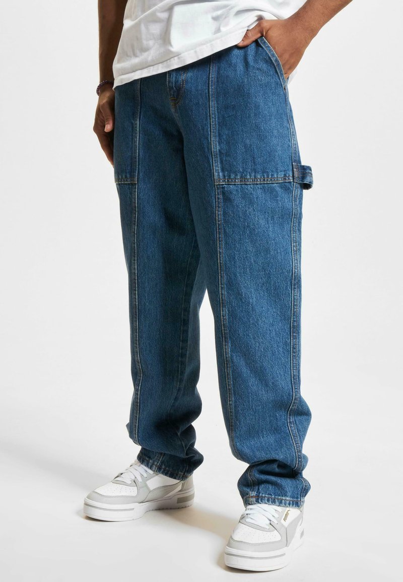 Denim cargo byxor i mellanmörk blå med en avslappnad passform, som har stora sidofickor, synlig sömnad och en mjuk tygstruktur.