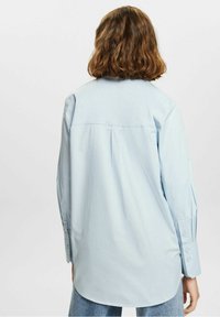 Ljusblå långärmad skjorta i mjukt tyg. Har en veckad rygg, knäppte ärmslut och en rundad nederkant. Enkel, klassisk design.