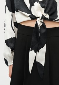 Μπλούζα με ασπρόμαυρο λουλουδάτο μοτίβο δεμένη κόμπος πάνω από τη μέση, σε συνδυασμό με μαύρο παντελόνι ψηλόμεσο.