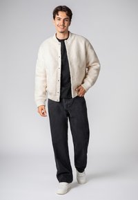Cream-colored, fluffy bomber jacket with a ribbed hem and cuffs, paired with a black shirt and dark jeans, worn with white sneakers.