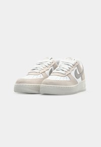 Hvide og beige Nike Air Force 1 sneakers har materialer af ruskind og læder, rund tå, flade snørebånd og et præget logo på tungen.